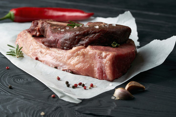 Raw fresh meat on paper with herbs, pepper and garlic on dark background