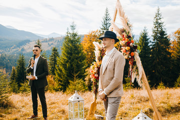 The groom stands under the wedding arch awaiting his wife