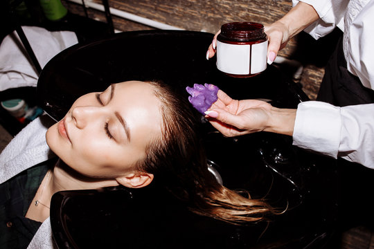 Close up face of beautiful young smiling woman getting hair care procedures in beauty salon, her eyes are closed with relaxation. Hair care, beauty products, spa