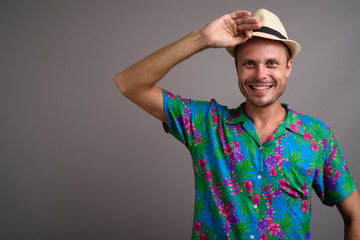 Portrait of handsome tourist man wearing hat ready for vacation against gray