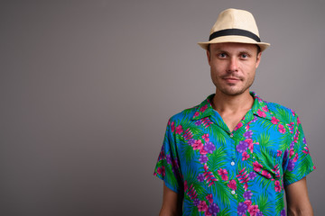Portrait of handsome tourist man wearing hat ready for vacation against gray