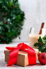 Beautiful gold present box with red bow and ribbons, ball, eggnog and holly berry branches on the background, stone table. Christmas and New Year concept