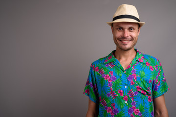 Portrait of handsome tourist man wearing hat ready for vacation against gray