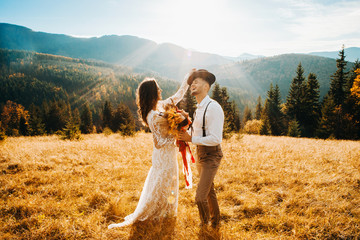 The bride in a white dress corrects the groom's hat at sunset. Mountain wedding in the rustic