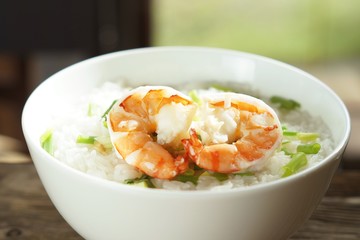 Traditional Thai porridge rice gruel and shrimp in a bowl with steaming on wooden table 