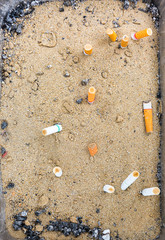 Cigarette burning in outdoors ashtray with sand