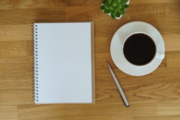 Obraz na płótnie Canvas Blank open notebook next to coffee cup on wooden table with copy space that you can mock up your text for art work design. 