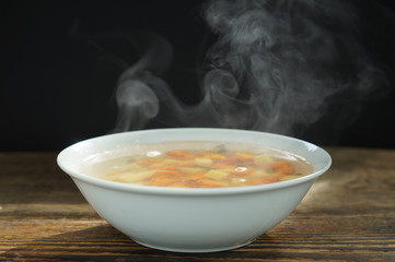 bowl of hot soup with steaming on wooden table on black background. Hot food consept.