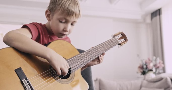 Young boy with a guitar. Boy of 8 years plays the classical guitar. The caucasian child learns to play the guitar. .Real time. Zoom in. Natural lighting. Low angle view.