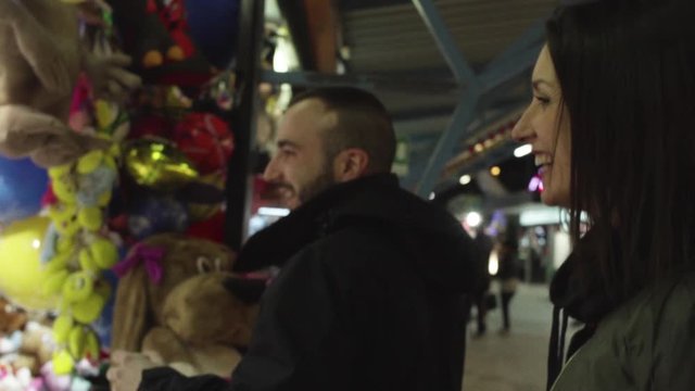 coppia al luna park con maschio che gioca al tiro a segno e femmina che fuma