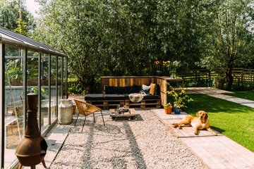 Green botanical garden with greenhouse, relaxing dog, gravel and grass.