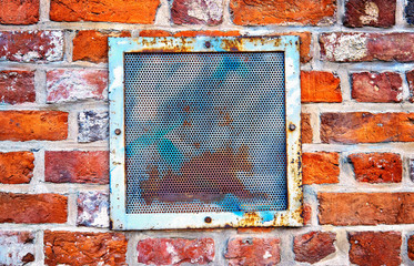 Metal ventilation grille in a red brick wall.