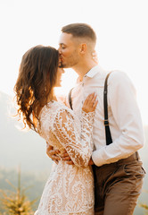 Stylish groom hugging happy bride in sun light, romantic moment, boho wedding couple, luxury ceremony at mountains with amazing view © Yuliia