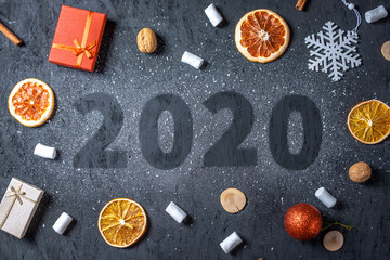 Card with numbers 2020 for New year and Christmas. Marshmallows and circles of orange and gift boxes on black background