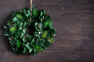 Christmas decoration wreath of green leaves and berries holly ilex plant isolated on dark wooden...