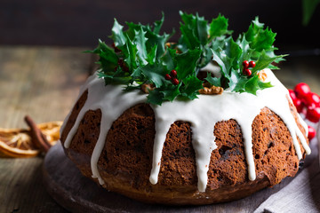Christmas homebaked dark chocolate bundt cake decorated with white icing and holly berry branches close-up