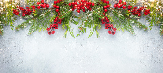 Christmas or winter background with a border of green and frosted evergreen branches and red berries on a grey vintage board. Flat lay