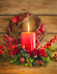 Burning Christmas red candle and  festive Christmas arrangement on a wooden table.