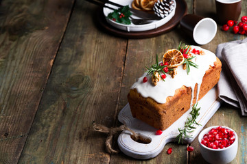 Fruit cake dusted with icing, nuts, kernels pomegranate and dry orange on old wooden background. Christmas and Winter Holidays homemade cake