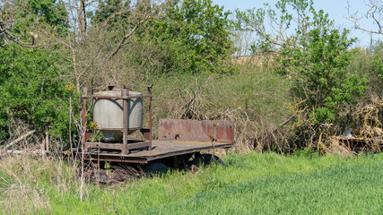 Ingrown rusty old tractor trailer in high green grass an trees