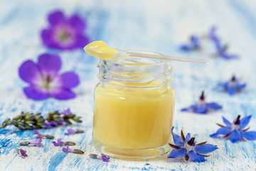 Raw organic royal jelly in a small bottle with litte spoon on small bottle surrounded by flowers.