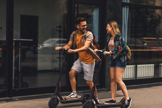 Young couple on vacation having fun driving electric scooter through the city.