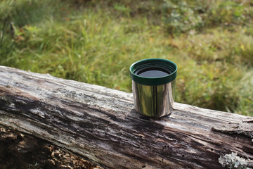 Thermos green plastic stainless steel mug on a log