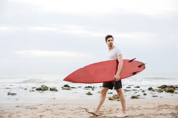 Handsome man surfer with surfing on a beach outside.