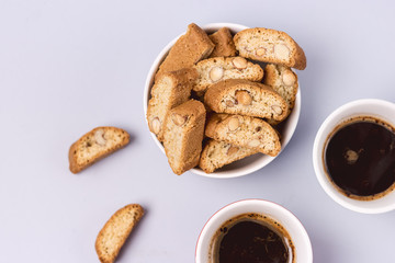 Italian Almond Biscuit Biscotti or Cantuccini in a White Bowl and Two Cups of CoffeeTasty Italian Dessert for Coffee or Wine Top View Blue Background