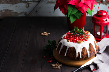 Christmas chocolate cake with white icing and pomegranate kernels on a wooden dark background with red lantern and poinsettia