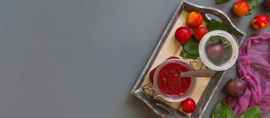 Juicy red plum and plum jam in white utensils and purple runner on gray laconic background pattern with copy space for text flat  lay top view