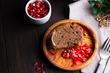 Christmas sliced chocolate cake with white icing and pomegranate kernels on a wooden dark background, flat lay