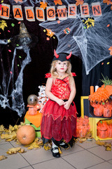 A child, a little girl in the shape of a witch on a broomstick, poses against the backdrop of scenery of cobwebs, pumpkins and autumn leaves on a Halloween holiday.