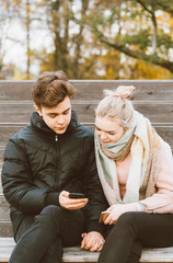 Loving teenagers on date look at mobile phones, guy shows the girl something interesting on phone. Immersion in virtual world, social networks. Concept of teen love, Smombie dating, vertical