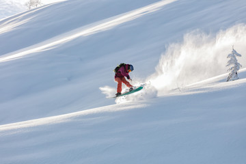 freerider in a bright suit rides fast skiing with large splashes of snow on a sunny day. Young Beautiful female skier. Snow scoot. Extreme winter sports. sunrise light, edit space. 