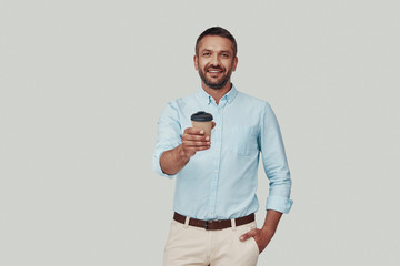 Handsome young man giving you drink and smiling while standing against grey background
