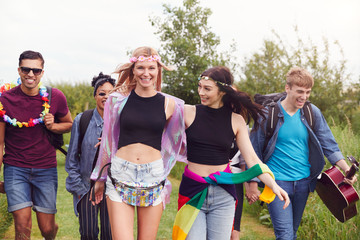 Group Of Excited Young Friends Carrying Camping Equipment Through Field To Music Festival