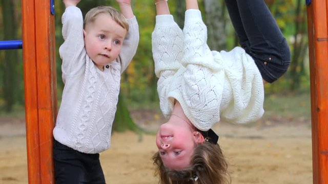 Brother and sister on horizontal bars. Girl hanging on the horizontal bar.
