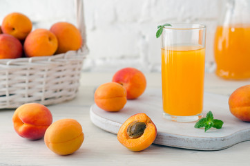 Glass with apricot juice and apricot fruits in basket on light background