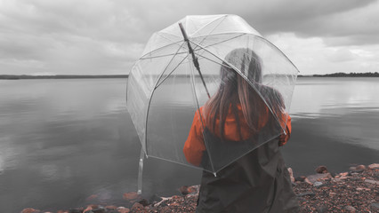 Girl on the lake with an umbrella in bad weather