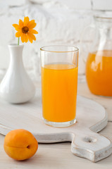 Glass with apricot juice and vase with yellow flower
