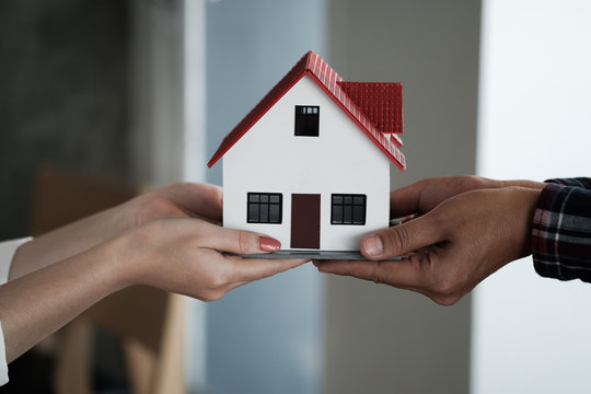 Real estate agent holding house model and pass to customer, Property concept.