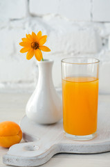Apricot juice in glass and vase with yellow flower