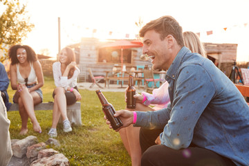 Group Of Young Friends At Music Festival Sitting Outside And Drinking Beer