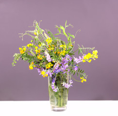 a bouquet of wild flowers is on the table in a glass of water on a gray background