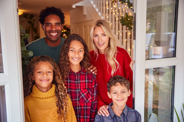 Portrait Of Family Standing In Open Front Door Of House On Christmas Day