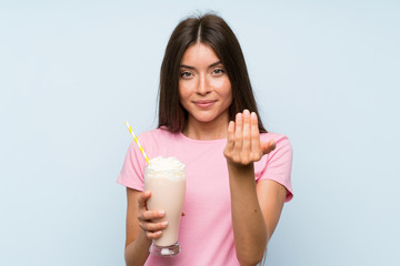 Young woman with strawberry milkshake over isolated blue background inviting to come with hand. Happy that you came