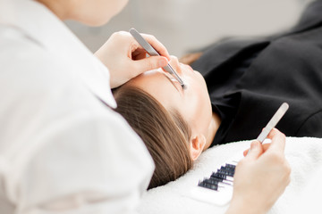 Obraz na płótnie Canvas Eyelash extension procedure. Master tweezers sets fake lashes on beautiful woman
