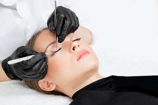 Eyelash extension procedure. Master tweezers fake long lashes beautiful female eyes