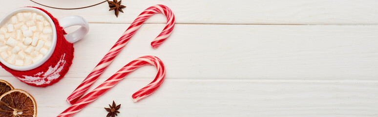 top view of christmas candy canes and cup of cocoa with marshmallows on white wooden table